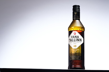 A bottle of Vana Tallinn is centered against a gradient background, transitioning from dark to light gray. The bottle has a textured cap and label detailing the brand and alcohol content, marked as 40. The design is classic with a focus on elegance and simplicity.