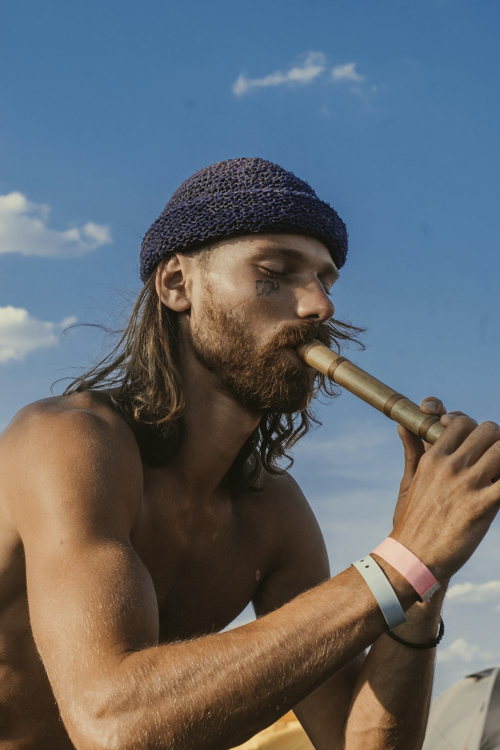 topless man playing flute under blue and white skies during daytime