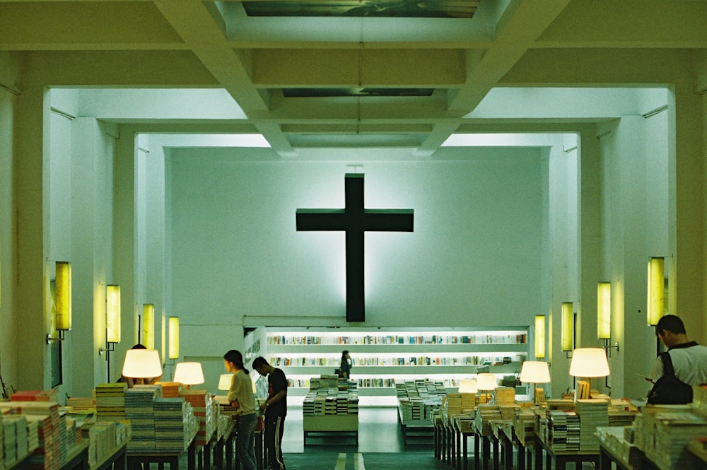 people standing inside building with black cross on wall
