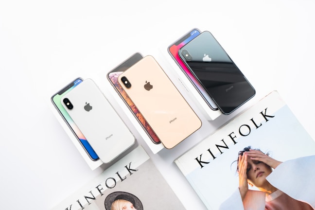 Several iPhones in different colors are displayed on their boxes beside a Kinfolk magazine featuring a person on the cover.