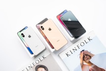 Several iPhones in different colors are displayed on their boxes beside a Kinfolk magazine featuring a person on the cover.