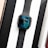 A black smartwatch with a digital clock display showing hands on a gradient blue and black background. It is placed on a white surface between a boxed phone labeled 'iPhone' and another boxed item with a visible wooden texture.