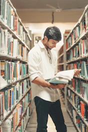 man holding and reading book while standing inside library