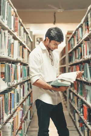 A man reading a book while standing in a university library, like a returning student catching up on coursework to finish a bachelor's degree at UNLV