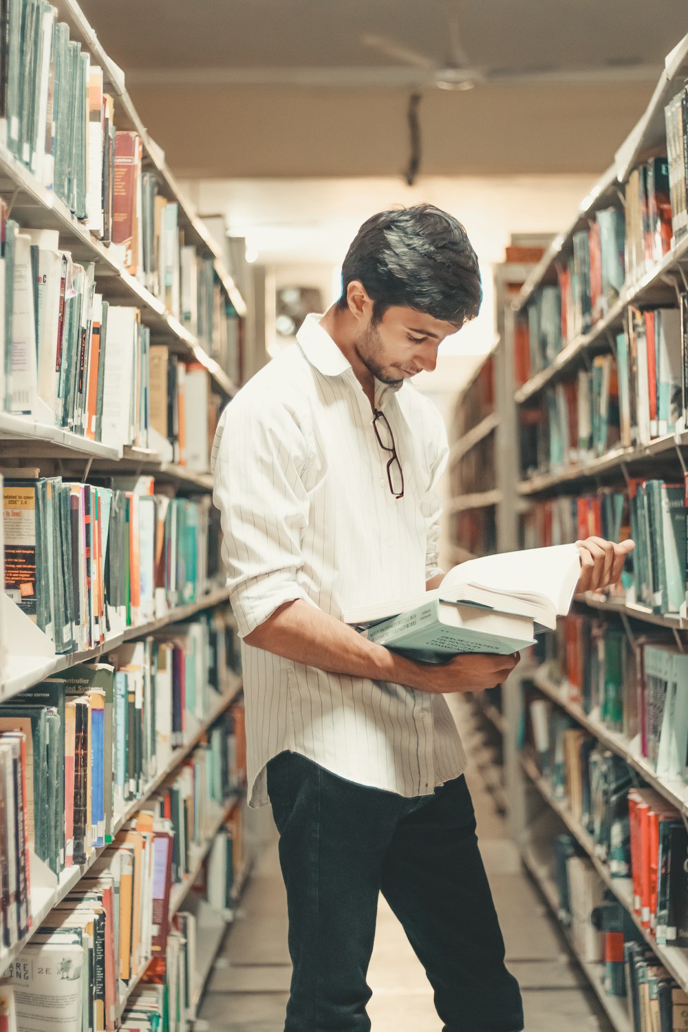 man holding and reading book while standing inside library