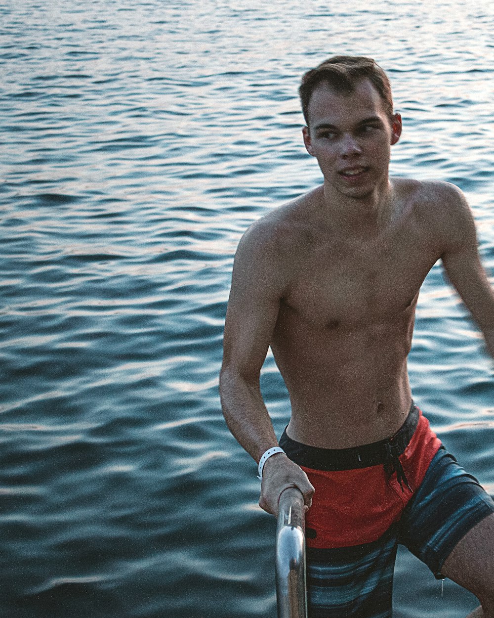 man wearing red and blue shorts while holding metal rail near body of water