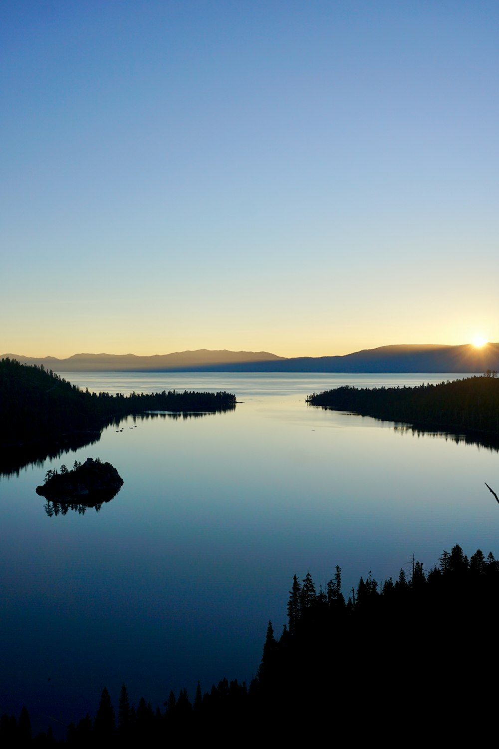 the sun is setting over a lake surrounded by trees