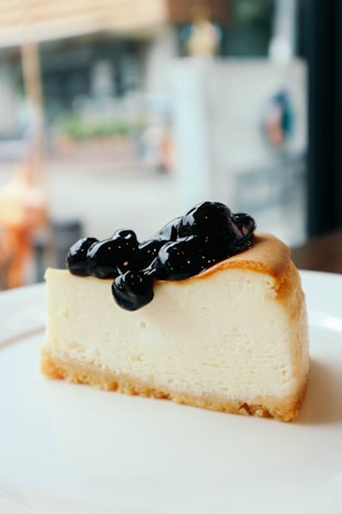 A close-up of a slice of creamy New York–style cheesecake topped with fresh berries and a drizzle of sauce.