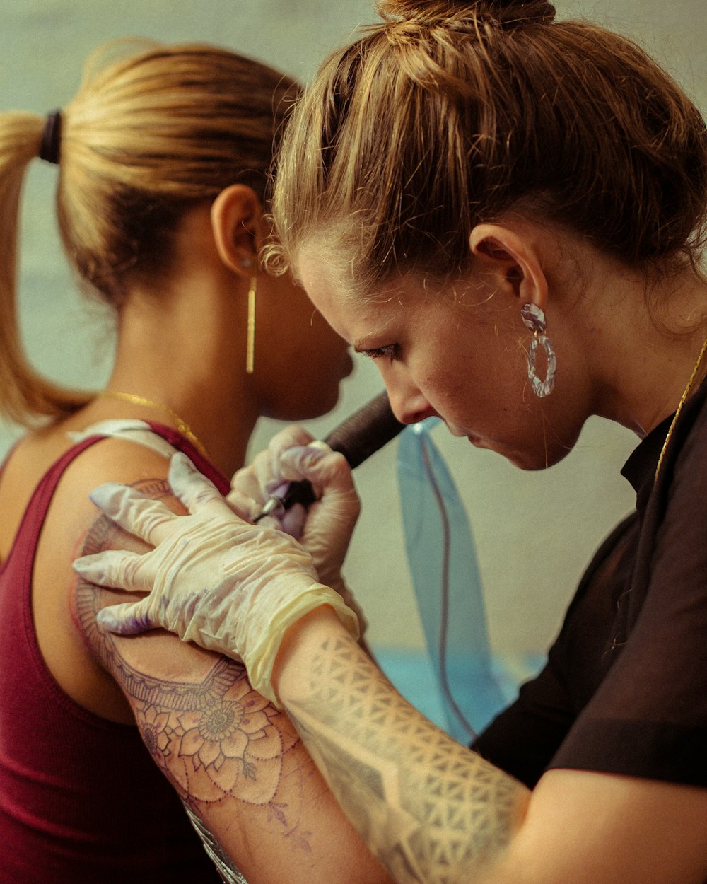 mulher tatuando outra mulher em seu ombro