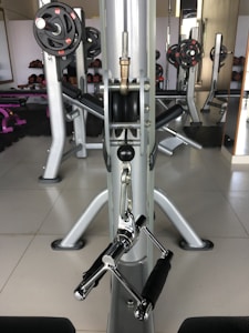 A gym setting with workout equipment including weights and a pulling mechanism. There are various weightlifting machines and plates organized in the background.