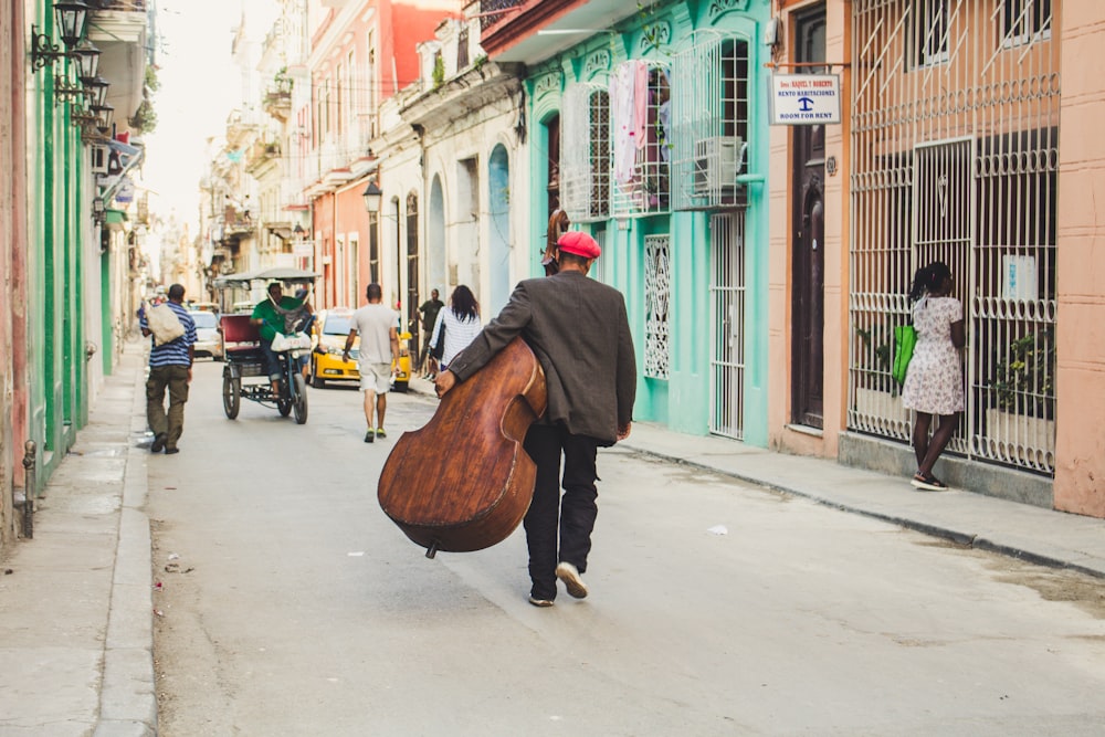 Homme portant un instrument à cordes en marchant sur le trottoir pendant la journée