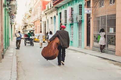 man carrying stringed instrument while walking the pavement during daytime