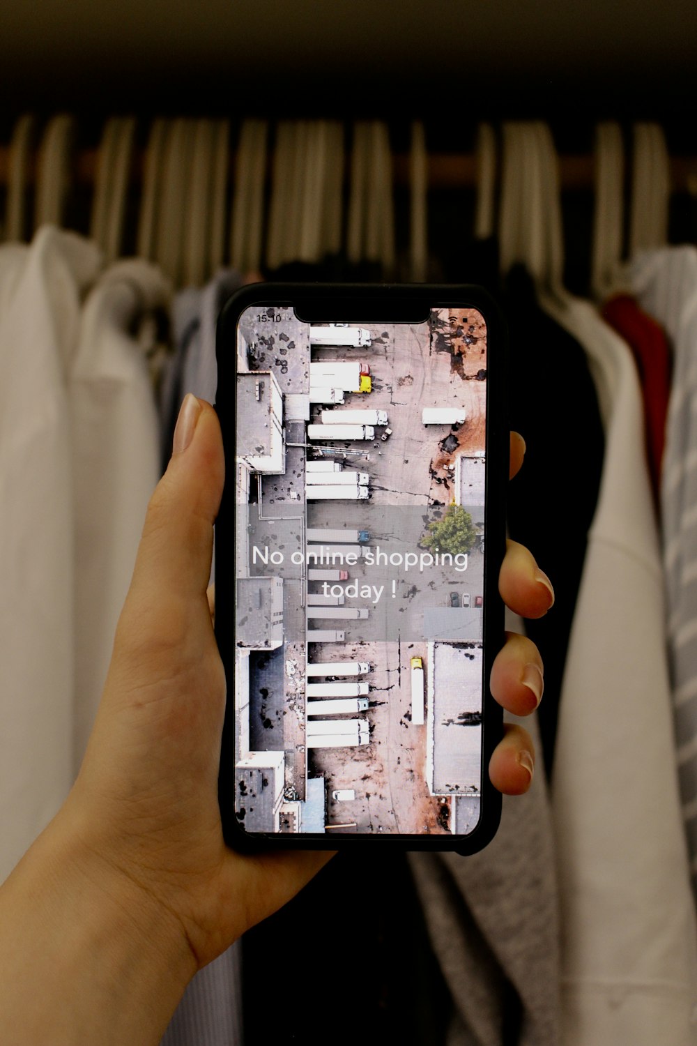 a person holding a cell phone in front of a rack of clothes