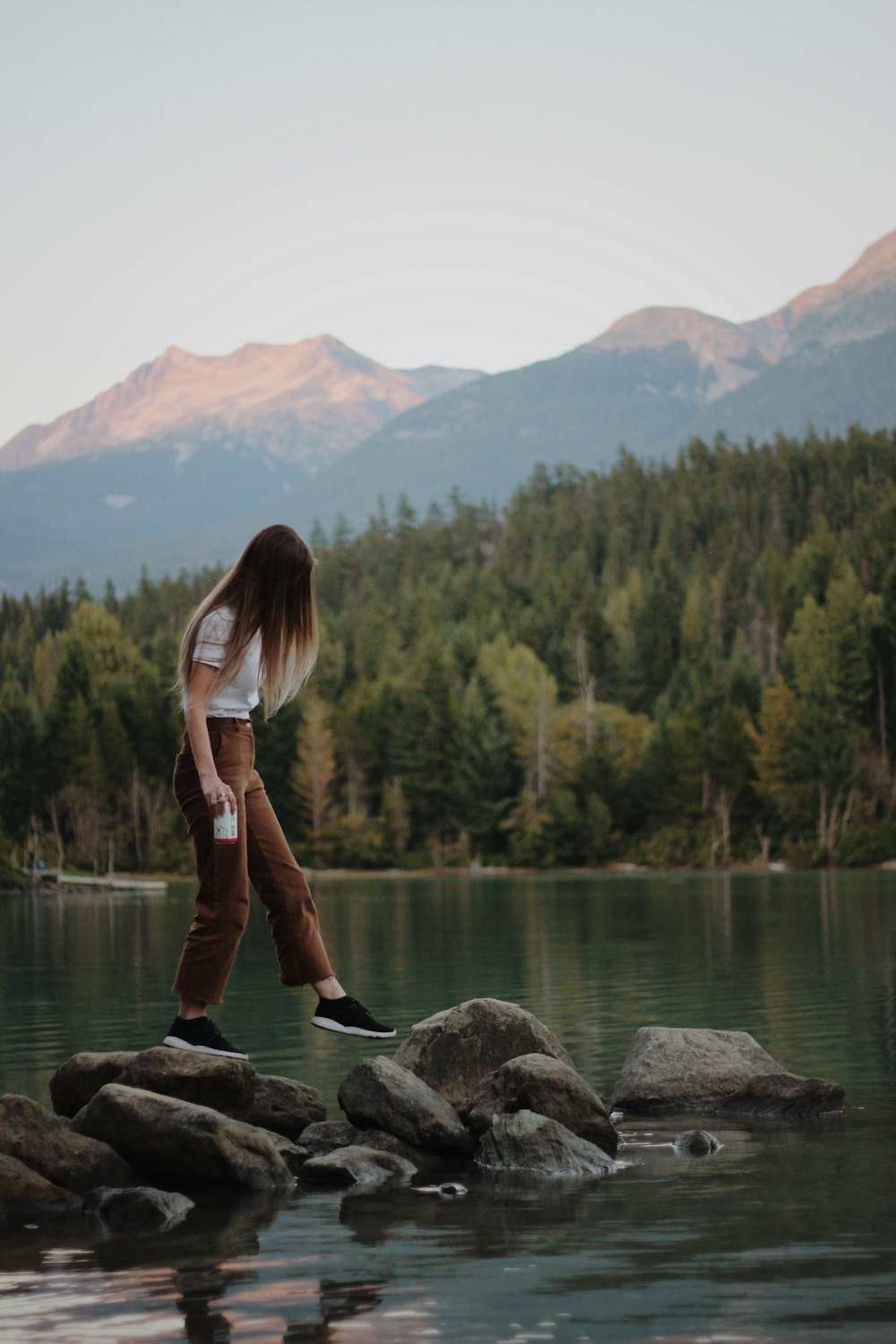 femme marchant sur des rochers gris près de la montagne d’observation du lac pendant la journée