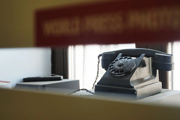 A vintage rotary phone resting on a wooden desk with soft sunlight filtering through a nearby window.