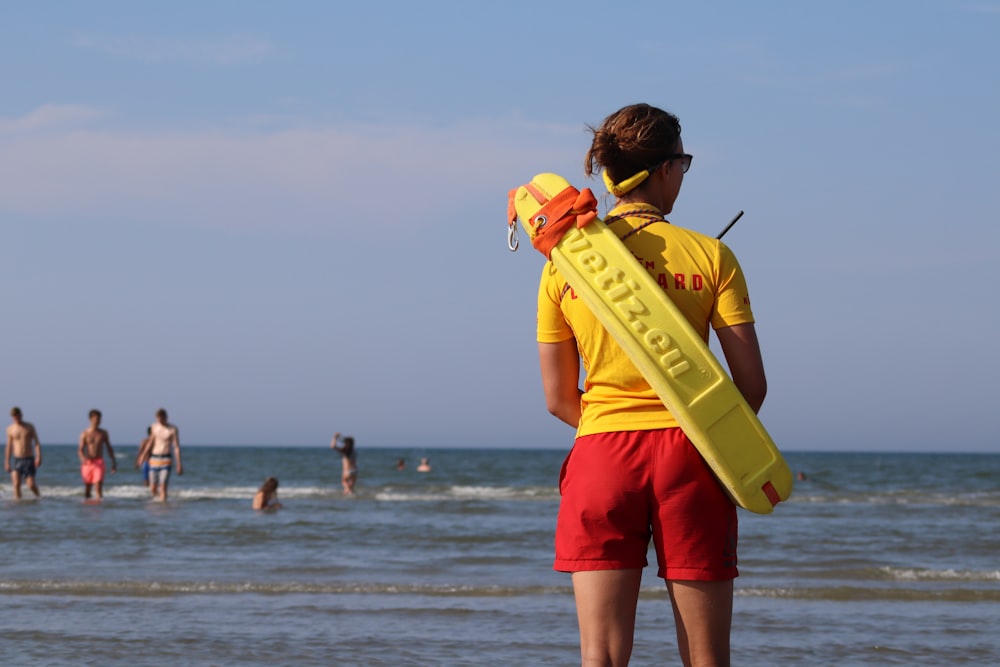 personne portant une planche de sport debout sur le rivage