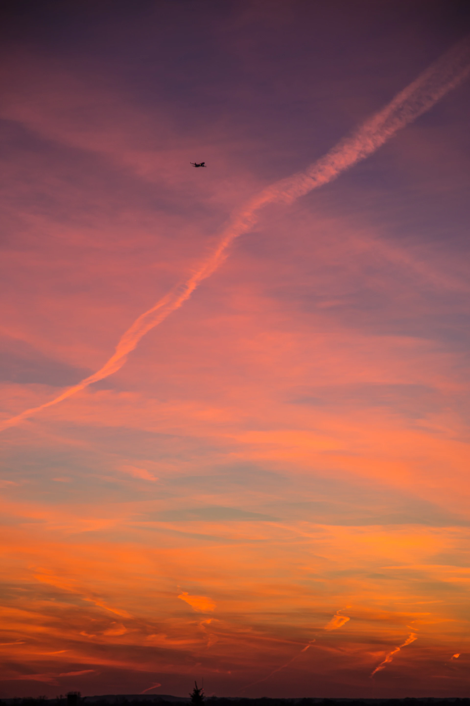A breathtaking sunset sky painted with shades of orange, pink, and purple, with a silhouette of a small airplane gliding through.