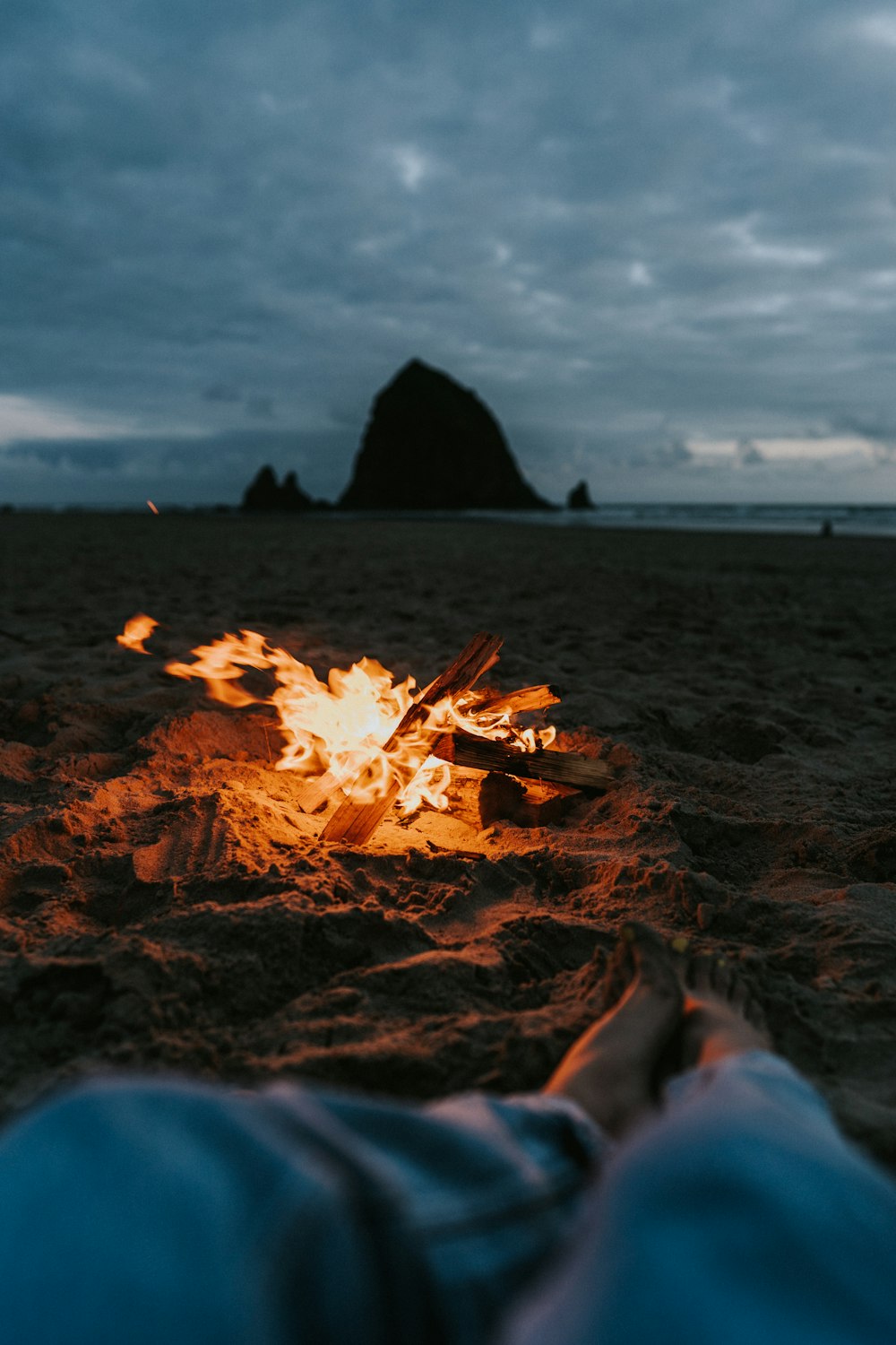 eine Person, die an einem Strand neben einem Lagerfeuer liegt