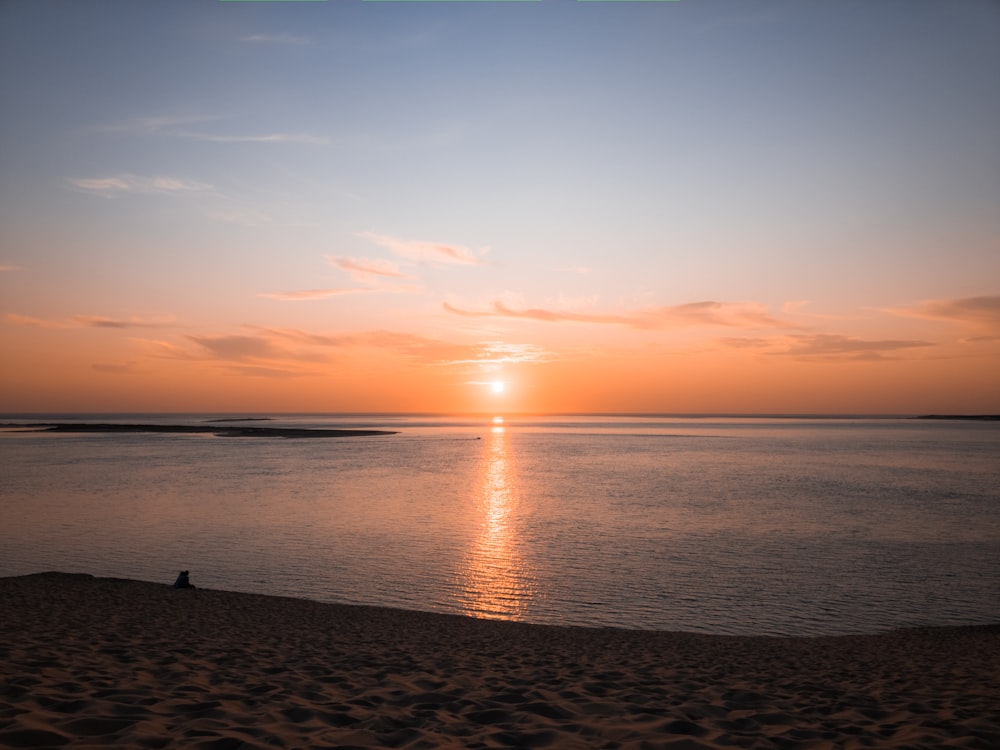 uma pessoa sentada em uma praia observando o pôr do sol