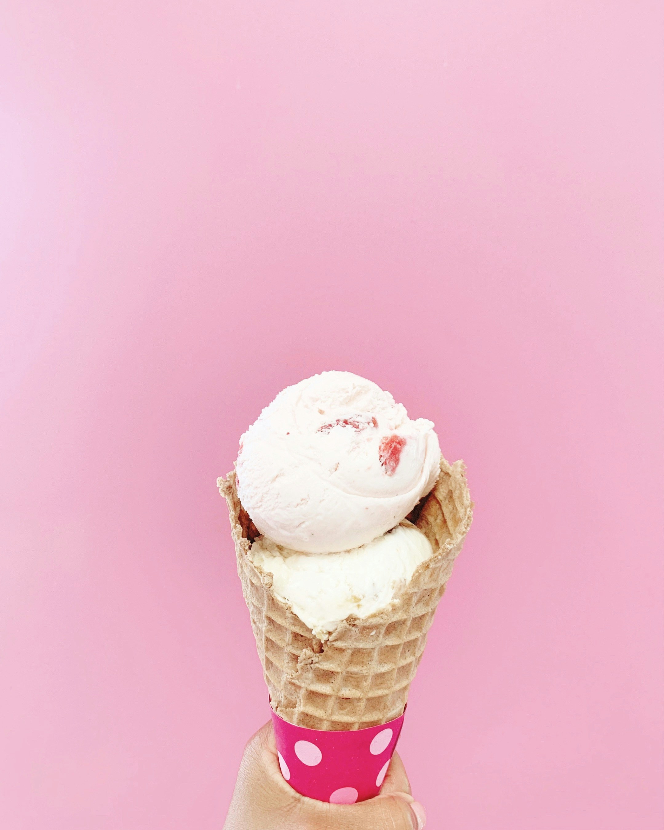 Scoops of pink strawberry ice cream in a waffle cone with caramelized nut topping, bright pastel background