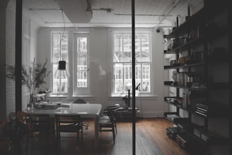 a room with a table, chairs, bookshelves and a window