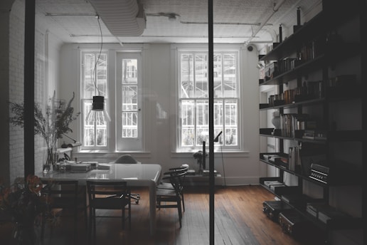 a room with a table, chairs, bookshelves and a window