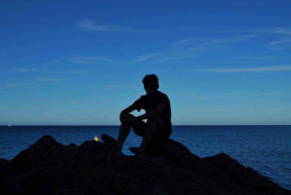 a man sitting on top of a rock next to the ocean