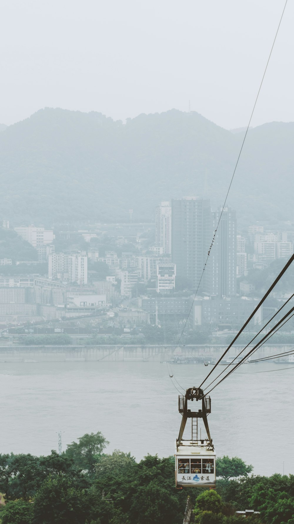 a cable car going over a river with a city in the background