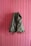 A green backpack hangs against a vertically paneled pink wooden wall. The backpack has leather straps and an overall rugged appearance, suggesting it is meant for outdoor use.