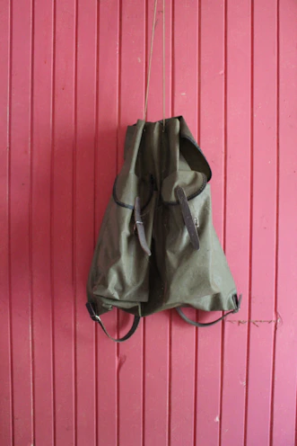 A modern leather backpack hanging on a minimalist hook against a neutral wall.