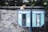 A ginger cat sits atop two old, blue public telephone booths that are attached to a stone wall. The booths are labeled 'Türk Telekom' and show signs of wear and graffiti. The surrounding area features greenery and a rugged stone texture.