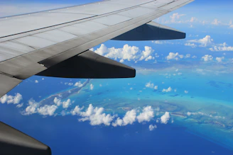 A scenic airplane wing view over turquoise ocean waters at sunrise.