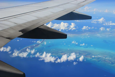 A scenic airplane wing view over turquoise ocean waters at sunrise.