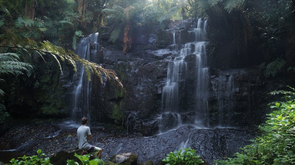 man sitting beside waterfalls