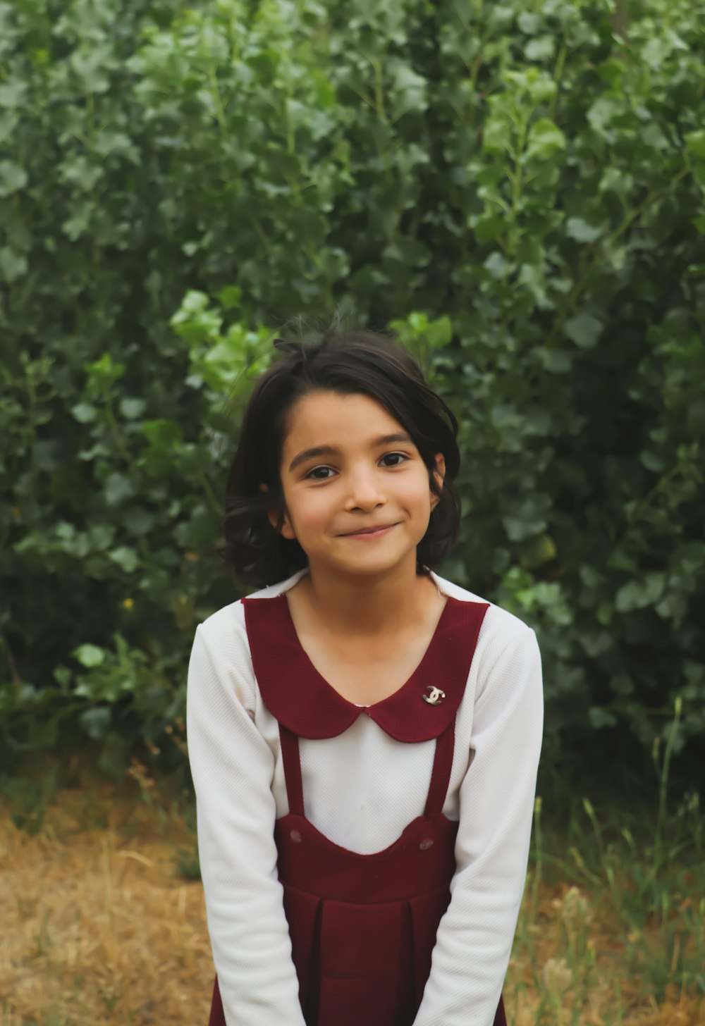 a young girl standing in front of a bush