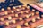 A selection of chocolate-covered eclairs topped with caramel popcorn is arranged neatly on a tray. The background shows a box containing pink macarons, adding a touch of color contrast.