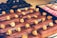 A selection of chocolate-covered eclairs topped with caramel popcorn is arranged neatly on a tray. The background shows a box containing pink macarons, adding a touch of color contrast.