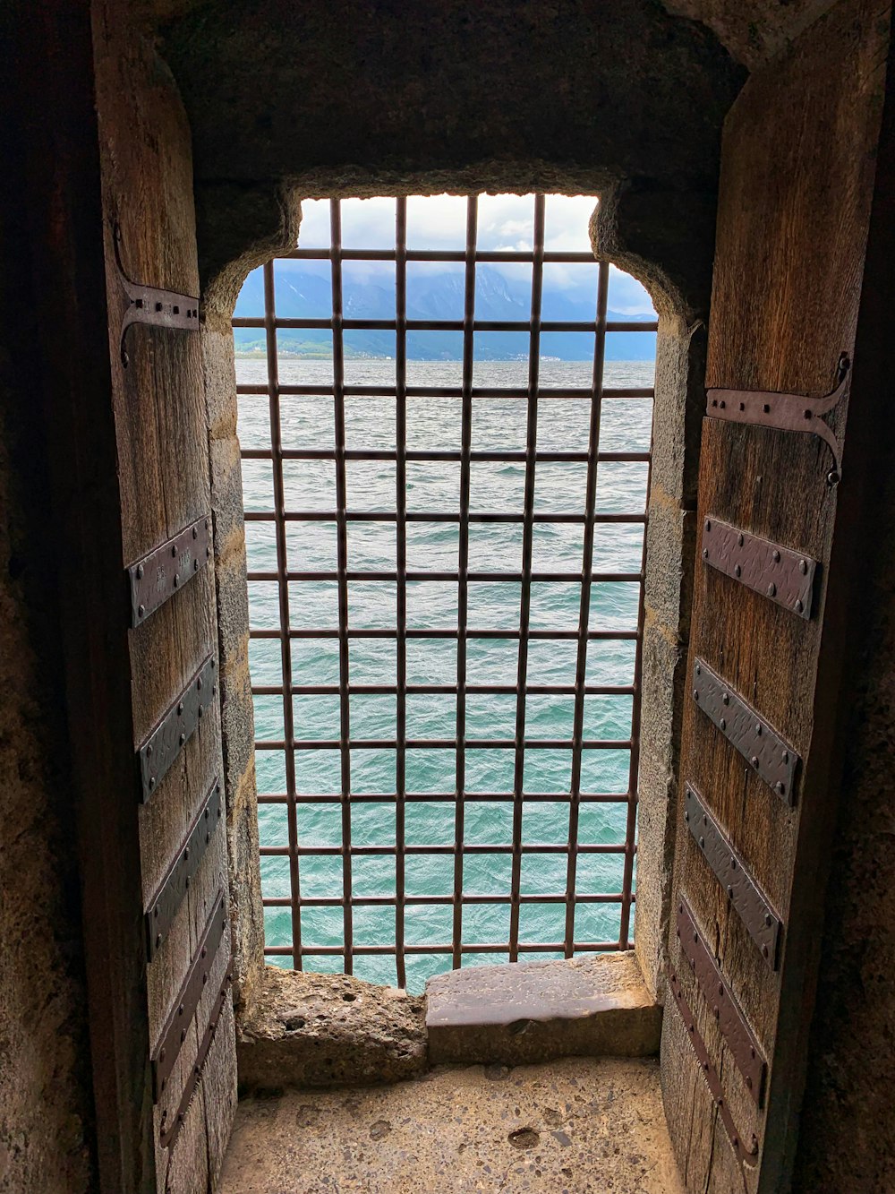 a window in a stone wall with a view of a body of water