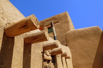 Adobe-style architecture with protruding wooden beams against a clear blue sky. The earthy tones of the building contrast with the vibrant sky, creating a warm, rustic feel.