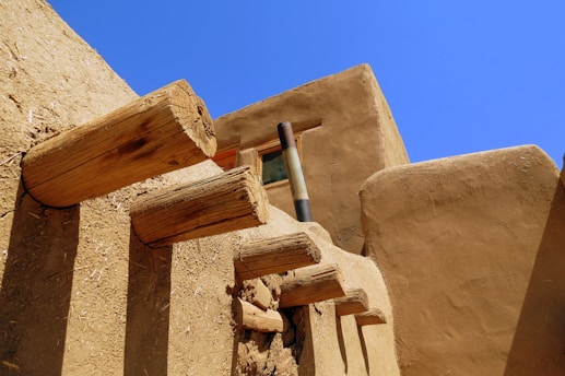 Adobe-style architecture with protruding wooden beams against a clear blue sky. The earthy tones of the building contrast with the vibrant sky, creating a warm, rustic feel.