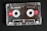 A transparent audio cassette tape with branding and labels displayed on a dark surface. The spools and magnetic tape are visible inside the clear plastic casing. Red labels with white text indicate the tape length and type.