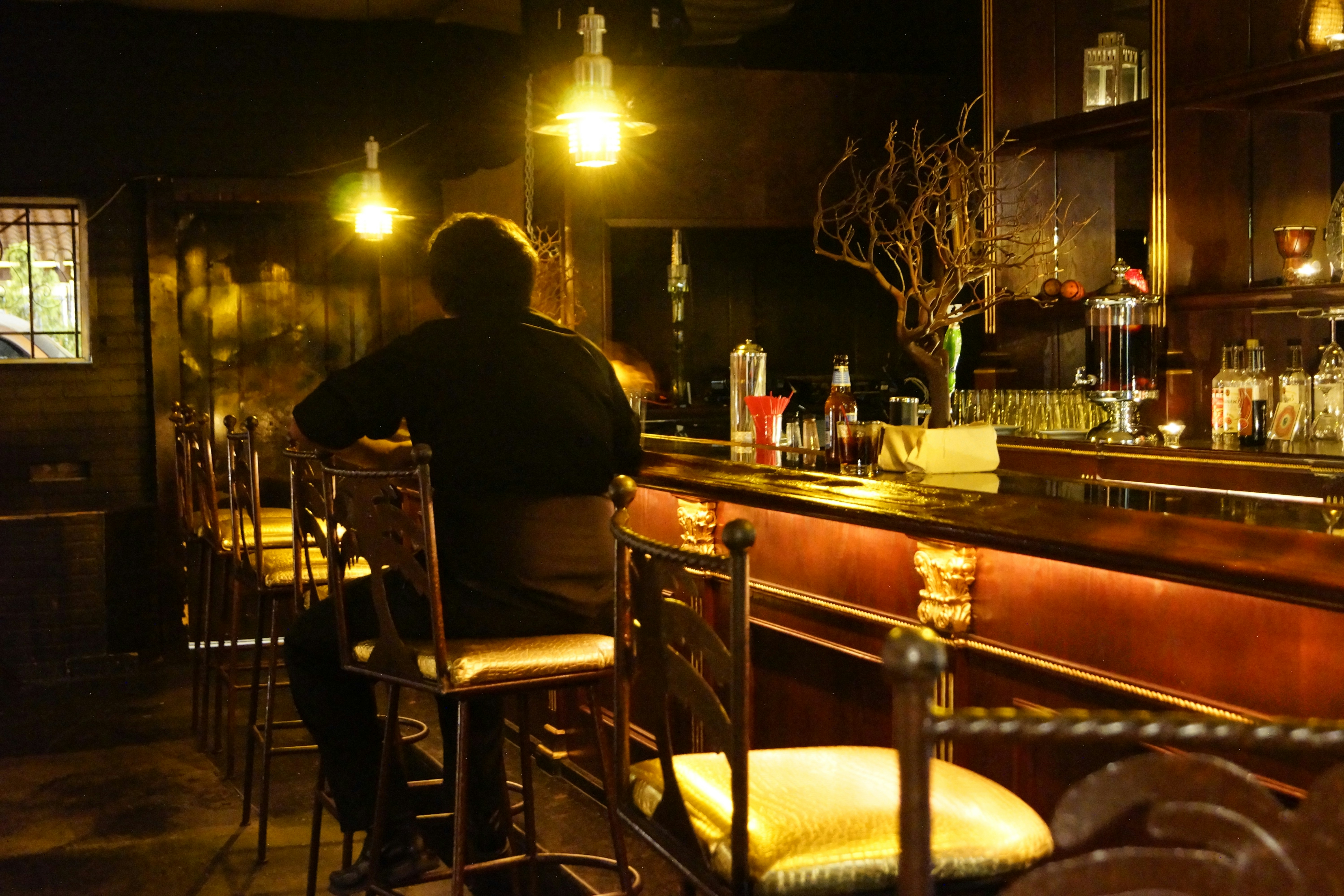 Man in his 30s sitting alone at a bar, looking thoughtful and introspective, moody dark lighting, cinematic atmosphere