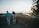 Two older adults stand by a stone wall overlooking a scenic landscape with a river, surrounded by trees and bathed in the warm light of a setting or rising sun.