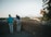 Two older adults stand by a stone wall overlooking a scenic landscape with a river, surrounded by trees and bathed in the warm light of a setting or rising sun.