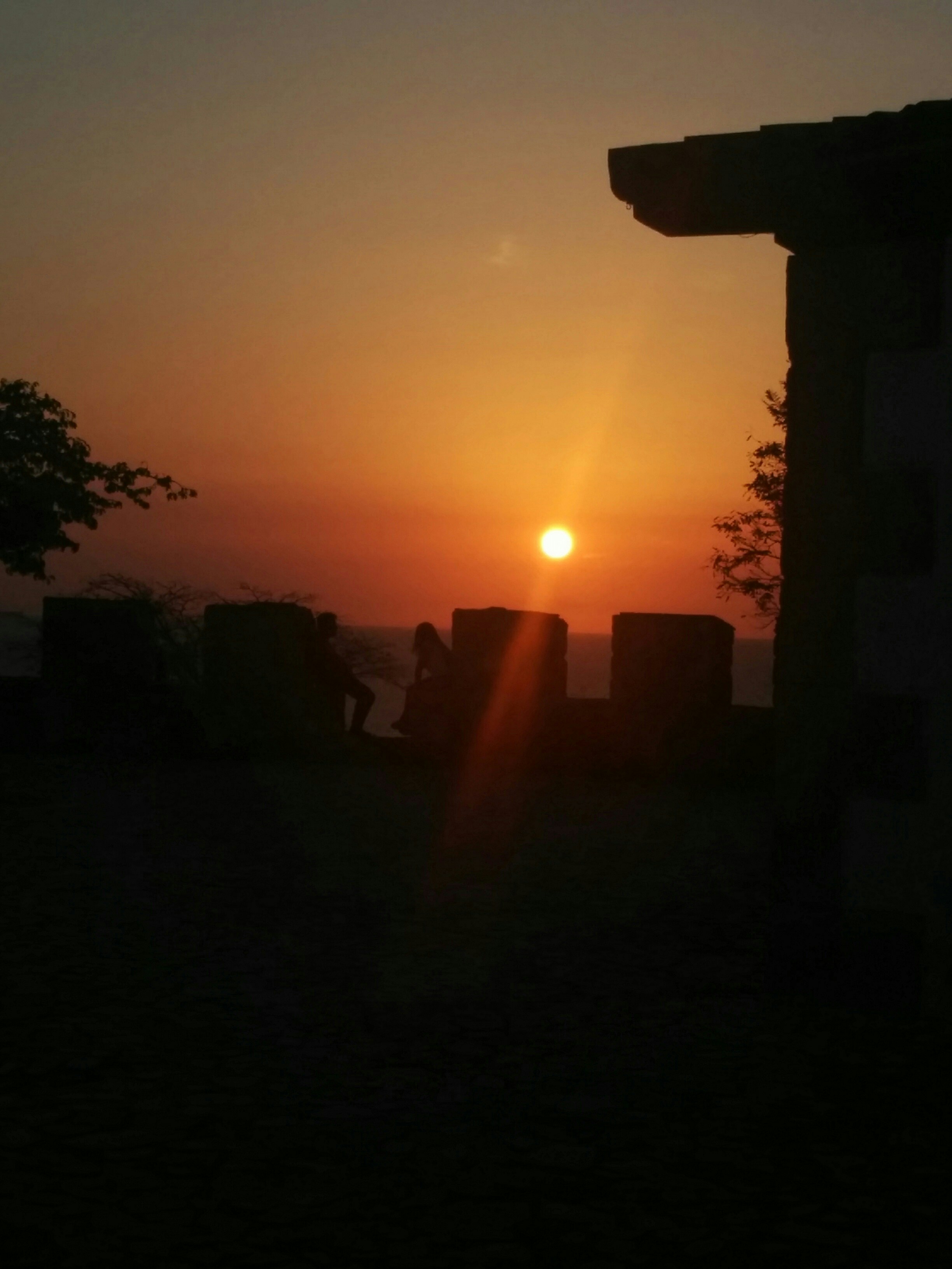 Ancient Omani fort silhouetted against warm desert sunset, deep shadows, dramatic Arabian landscape