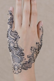 A hand with intricate black henna designs featuring floral and abstract patterns, delicately drawn on the back of the hand.