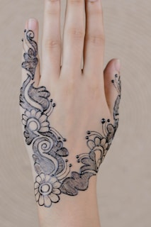 A hand with intricate black henna designs featuring floral and abstract patterns, delicately drawn on the back of the hand.