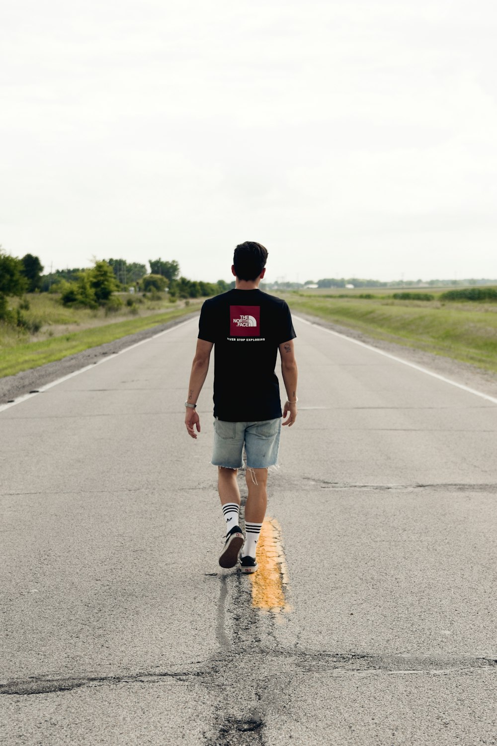 man walking black shirt and blue denim shorts