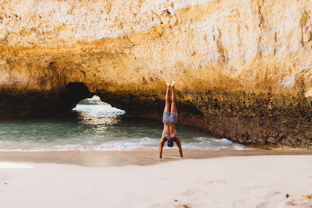 man doing stunt on seashore near rock formation