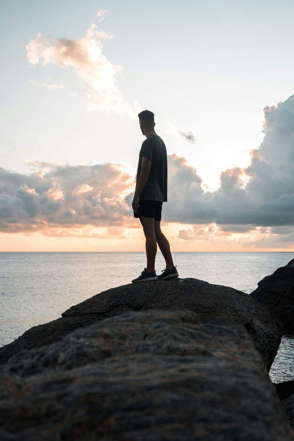man in black shorts standing on rock near sea during daytime